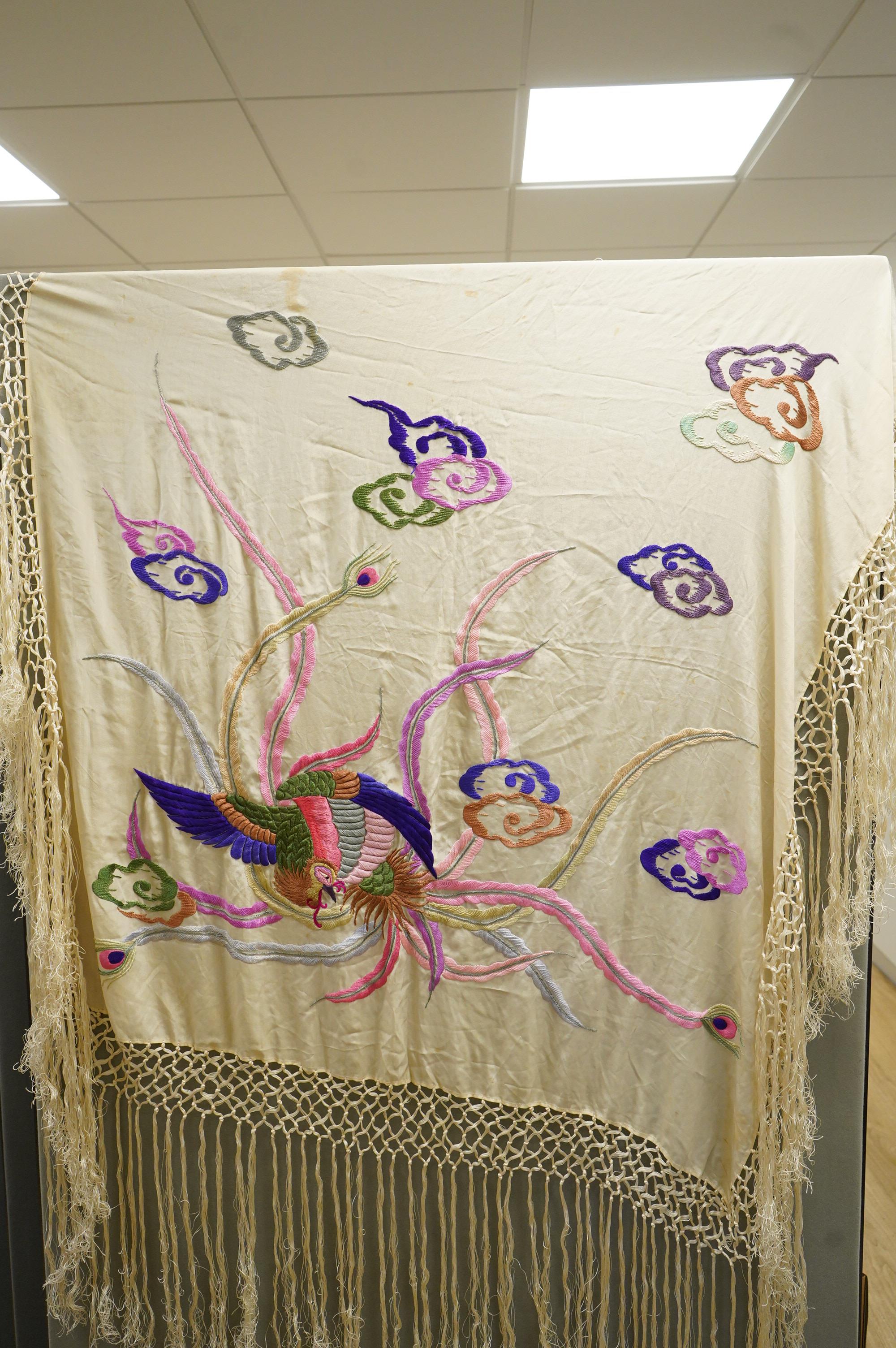 A unusual Chinese 1920’s-30’s cream silk fringed shawl, embroidered with a large central motif of a phoenix in flight, embroidered in bright multi coloured silks. 108cm x 100cm, Condition - there are some stains.